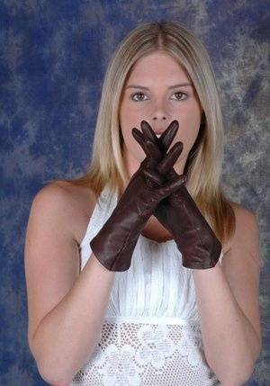 Blonde female pulls on brown leather gloves while wearing a white dress on fanspics.com