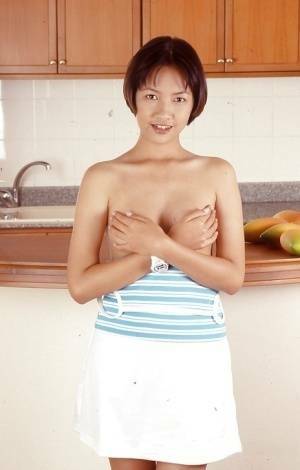 Clothed Asian with tiny tits is posing in the kitchen with spread legs on fanspics.com