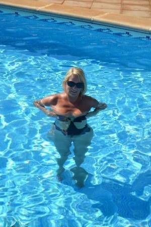 Middle-aged blonde Sweet Susi frees her tits & pussy from a swimsuit by a pool on fanspics.com