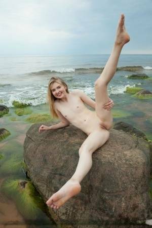 Slim teen Nimfa removes a black bikini to pose naked on seaside rocks on fanspics.com