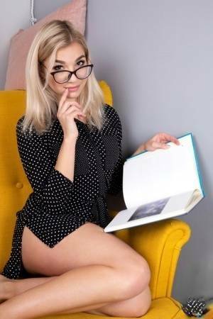 Geeky blonde Amelia undresses on a chair before playing with her shaved pussy on fanspics.com