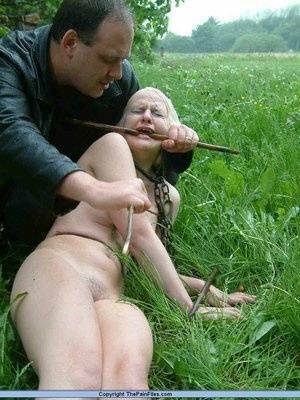 Naked blonde slave is caned and stomped on in a field of lush grass on fanspics.com