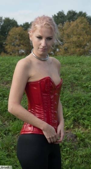 Collared girl Arienh Autumn models a red leather corset while in a field on fanspics.com