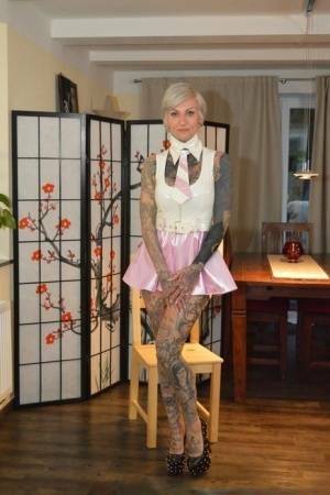 Tattooed platinum blonde Miss Francine models a raincoat over a latex dress on fanspics.com