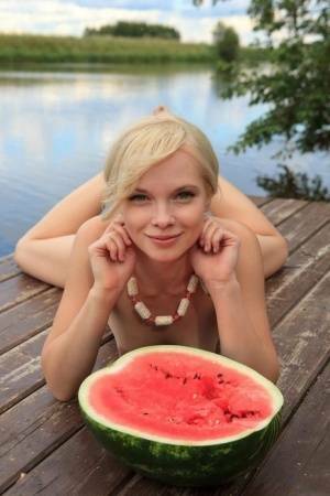 Beautiful blonde Feeona eats a watermelon while posing naked on lakeside dock on fanspics.com