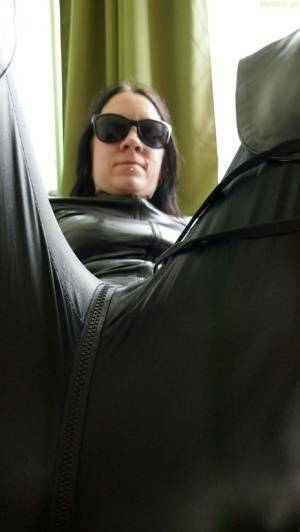 Dark haired amateur models a leather catsuit while wearing dark sunglasses on fanspics.com